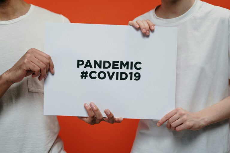 Two people holding a paper that says "Pandemic #COVID19."