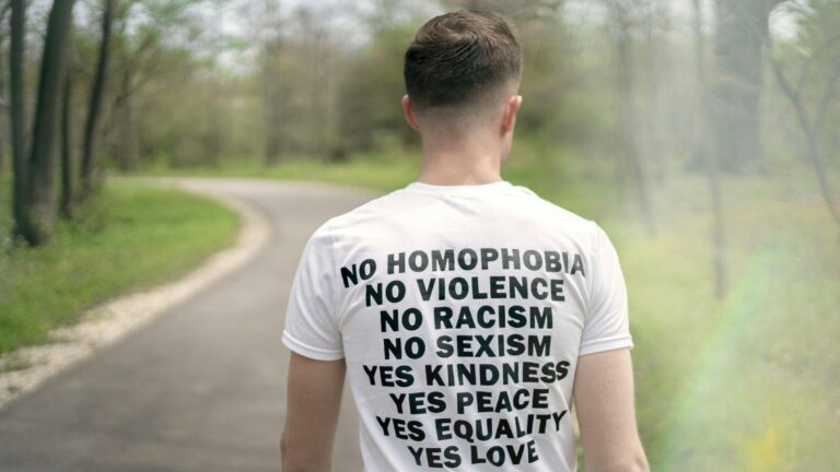A man wearing a tshirt that says, "No homophobia, no violence, no racism, no sexism, yes kindness, yes peace, yes equality, yes love."