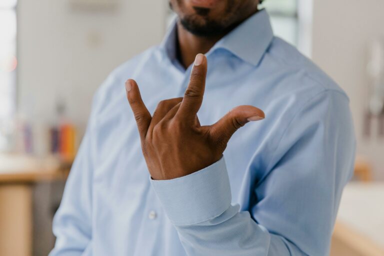A man holding up his pointer finger, pinky, and thumb to show three fingers.