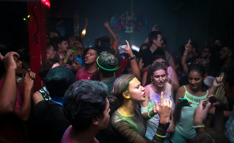 A crowd dancing with glowsticks and colored powder at a party.