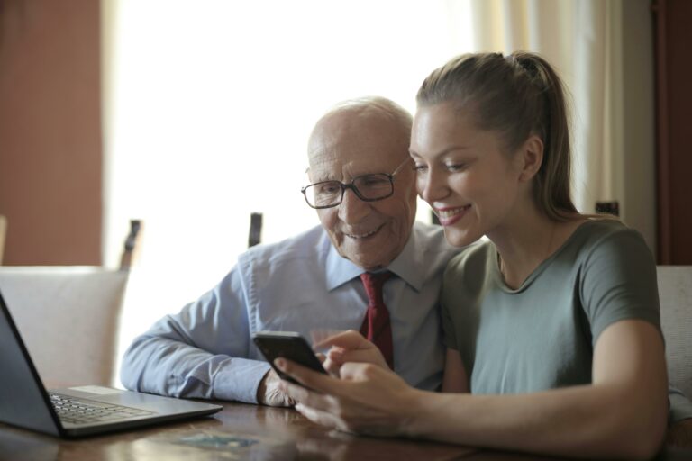 A young woman smiling while showing a senior man something on her smart phone.