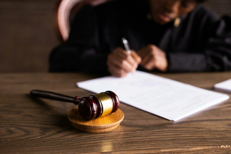 A person signing a document at a table with a gavel on it.