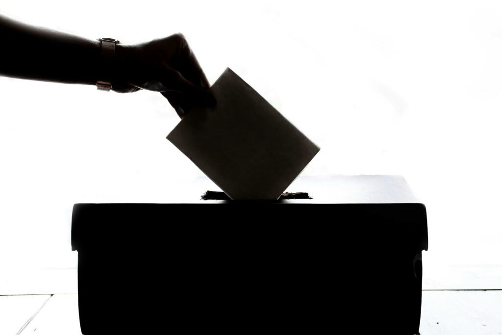 A hand casting a vote into a poll box.