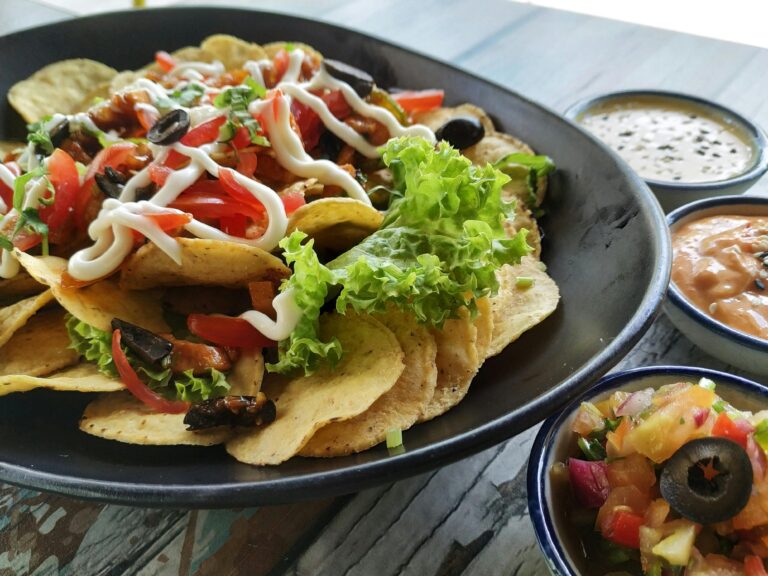 A bowl of tortilla chips covered in salsa and vegetables.